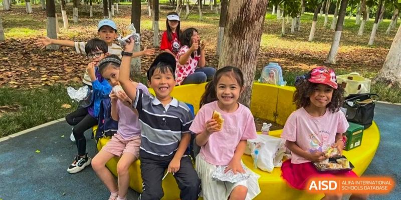 Two young students smile and wave while enjoying a meal together during an outdoor gathering at Ecole Française Internationale de Wuhan.