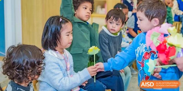 A group of young students sit together as one child carefully holds a handmade yellow paper flower at Ecole Française Internationale de Wuhan.