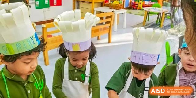 A young student wearing a tall, handmade paper chef's hat and apron during a classroom activity at Ecole Française Internationale de Wuhan.