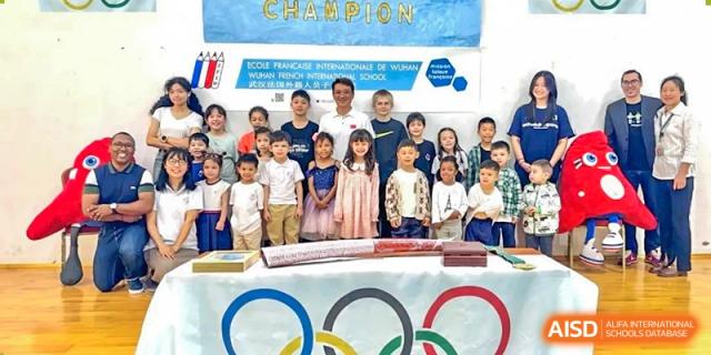 A large group of students and staff posing for a photo behind an Olympic rings banner and "Champion" sign at Ecole Française Internationale de Wuhan.