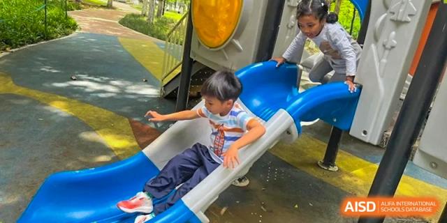 A young child smiling while sliding down a blue slide on the outdoor playground equipment at Ecole Française Internationale de Wuhan.