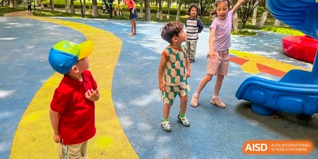 Children standing on a colorful blue and yellow patterned playground surface during a break at Ecole Française Internationale de Wuhan.