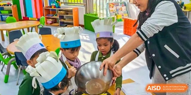 Two young students wearing paper chef hats work together to mix ingredients in a large metal bowl at Ecole Française Internationale de Wuhan.