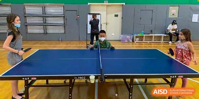 A young student in a green shirt focused on a table tennis match in the school sports hall at Ecole Française Internationale de Wuhan.
