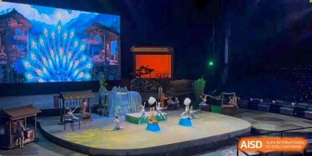 Students performing a choreographed dance on a brightly lit stage with a scenic digital backdrop at Ecole Française Internationale de Wuhan.