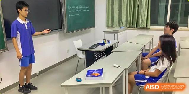 An empty classroom corner featuring a white desk with a blue book, a computer mouse, and a green chalkboard at Shenzhen Senior High School International Division.