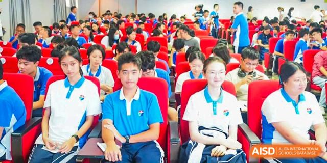 Two students, a boy and a girl, sitting in bright red auditorium chairs wearing white and blue polo shirts at Shenzhen Senior High School International Division.