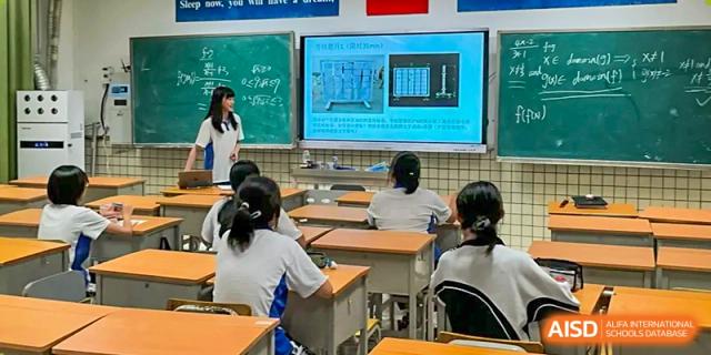 Students sitting at desks in a classroom looking at a large digital screen displaying a technical presentation at Shenzhen Senior High School International Division.