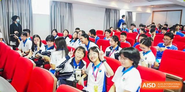 A group of smiling students in blue and white athletic uniforms sitting in a lecture hall with red seats at Shenzhen Senior High School International Division.