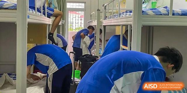 Students inside a dormitory room featuring metal bunk beds with blue and white bedding and storage lockers at Shenzhen Senior High School International Division.
