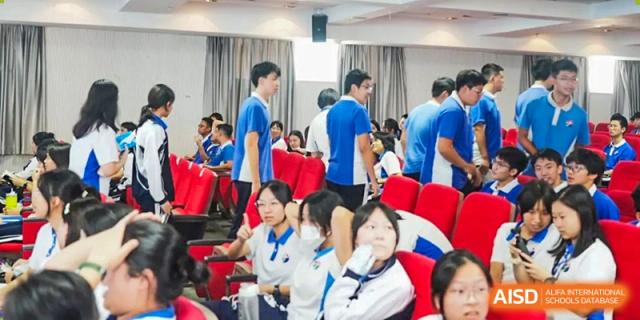 A busy indoor assembly or lecture hall with students in blue uniforms moving between rows of red velvet seats at Shenzhen Senior High School International Division.