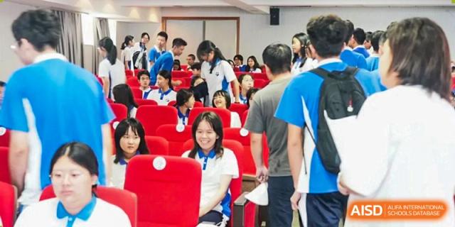Students gathering and talking in a large auditorium filled with rows of red seating during an event at Shenzhen Senior High School International Division.