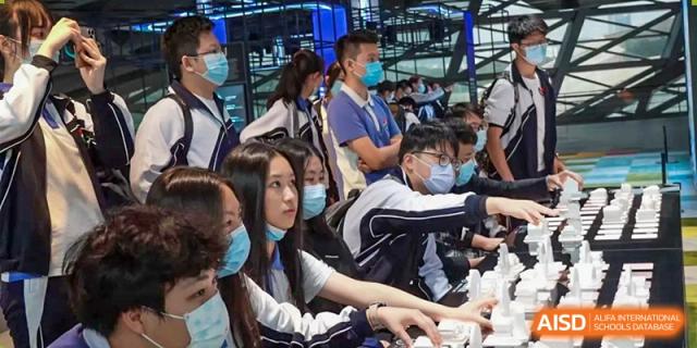 Students wearing face masks and school uniforms looking closely at a museum exhibit or architectural model at Shenzhen Senior High School International Division.