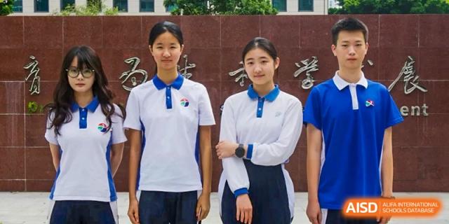 Two female students posing in white and blue polo shirts in front of a dark stone wall with gold inscriptions at Shenzhen Senior High School International Division.