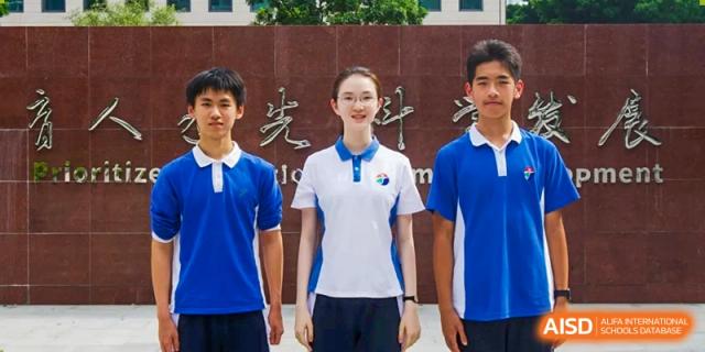 Three students standing in front of a stone monument with gold lettering wearing blue and white polo shirts at Shenzhen Senior High School International Division.