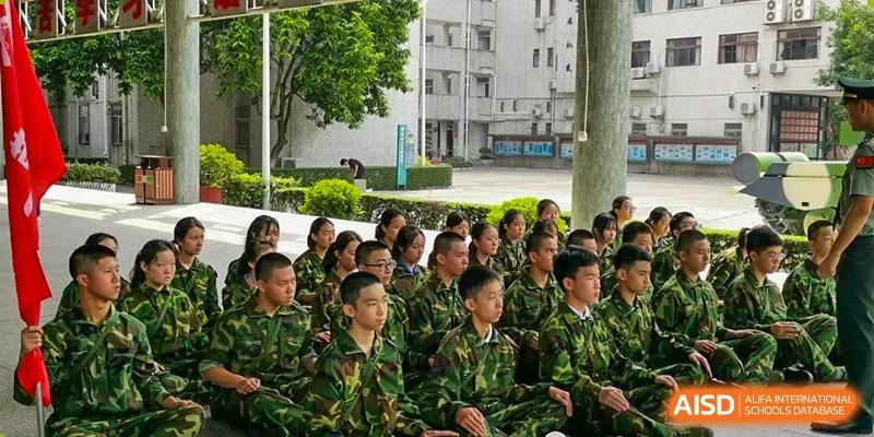 A large group of students wearing green camouflage uniforms sits attentively on the ground during an outdoor event at Shenzhen Senior High School International Division.