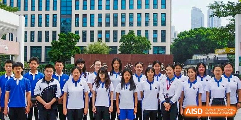 A group of female students in white and blue polo uniforms stands in front of a modern school building at Shenzhen Senior High School International Division.
