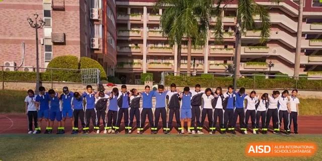 Students stand in a long line on a grassy field in front of a large brick campus building during the day at Shenzhen Senior High School International Division.