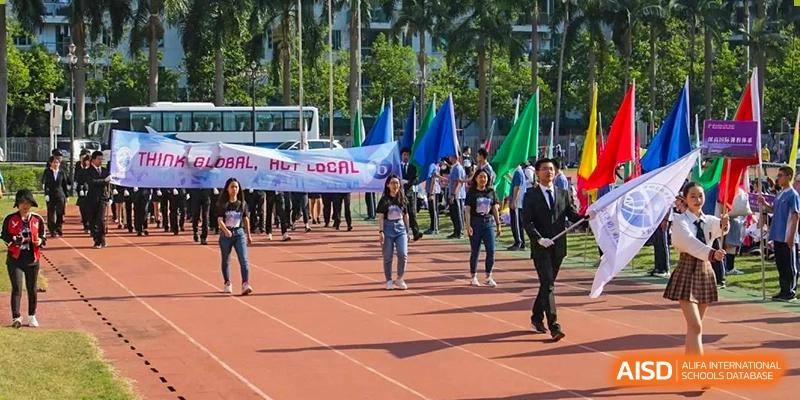 A group of students marches on an outdoor track holding colorful flags and a large banner during a school event at Shenzhen Senior High School International Division.