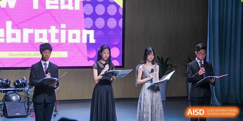 Two female students in elegant formal dresses stand on a stage holding microphones and scripts for a gala at Shenzhen Senior High School International Division.