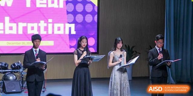 Two female students in elegant formal dresses stand on a stage holding microphones and scripts for a gala at Shenzhen Senior High School International Division.