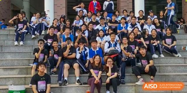 Large group of students sitting on outdoor bleachers, smiling for a group photo at Shenzhen Senior High School International Division.
