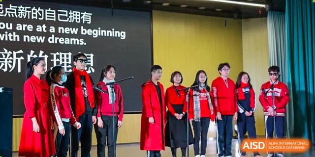 Five students standing on a stage wearing matching red and black outfits during a presentation at Shenzhen Senior High School International Division.