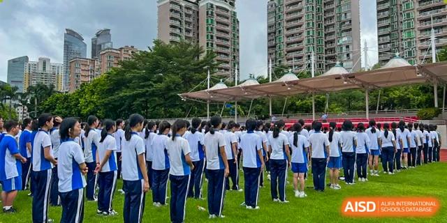 Students in blue and white uniforms standing in neat rows on a green field with buildings behind them at Shenzhen Senior High School International Division.