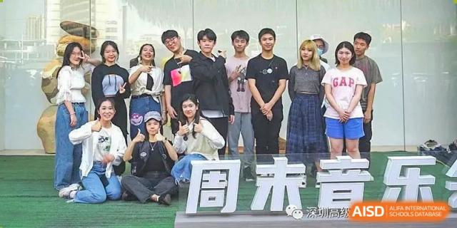 A group of students posing together behind a large white sign during an outdoor school event at Shenzhen Senior High School International Division.
