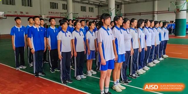 Students in blue and white athletic uniforms standing in formation on an outdoor court at Shenzhen Senior High School International Division.