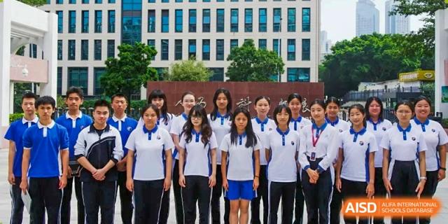 A group of students in matching white and blue polo shirts posing before a school building at Shenzhen Senior High School International Division.