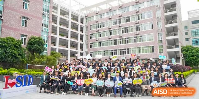 Large group of students and staff posing with colorful signs in front of a multi-story campus building at Shenzhen Senior High School International Division.