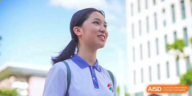 Low-angle portrait of a smiling female student wearing a white and blue polo uniform outdoors at Shenzhen Senior High School International Division.