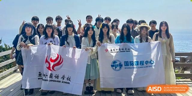 A group of students stands outdoors holding white school flags and making peace signs at Wuxi Foreign Language School International Curriculum Center.