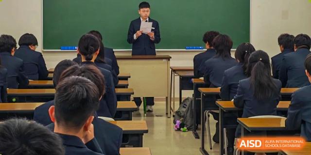 A student in a navy blazer stands at a podium in front of a chalkboard to give a presentation at Wuxi Foreign Language School International Curriculum Center.
