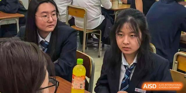 A female student in a formal school uniform sits at a desk during an indoor academic session at Wuxi Foreign Language School International Curriculum Center.