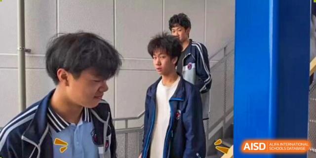 Two male students in blue and white school track jackets stand together outdoors in a candid moment from Wuxi Foreign Language School International Curriculum Center.