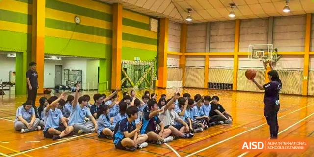 A large group of students in blue shirts sits on a gymnasium floor during an assembly at Wuxi Foreign Language School International Curriculum Center.