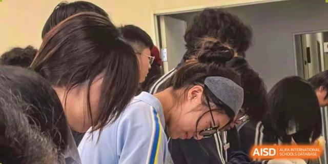 A student with a headband leans over to focus on a task during a hands-on classroom activity at Wuxi Foreign Language School International Curriculum Center.