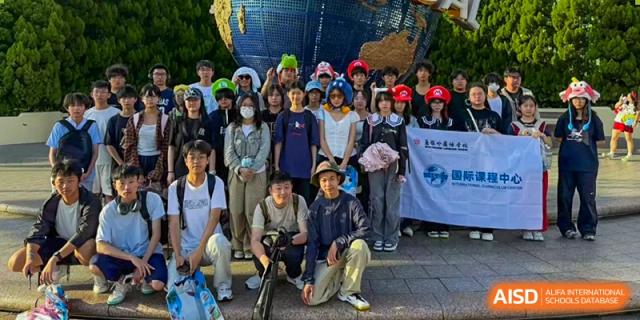 A large group of students posing in front of a blue globe at a theme park, many wearing Mario-themed hats, from Wuxi Foreign Language School International Curriculum Center.