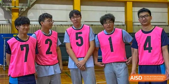 Two male students wearing pink numbered sports vests standing on a basketball court at Wuxi Foreign Language School International Curriculum Center.