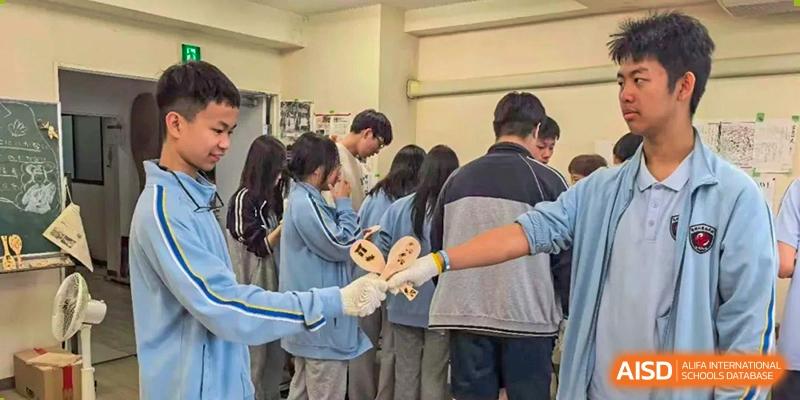 Students in blue uniforms hold up wooden paddle crafts during a creative workshop at Wuxi Foreign Language School International Curriculum Center.