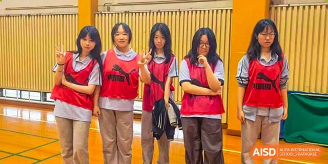 Three female students wearing red Puma sports bibs pose for a photo in a gymnasium at Wuxi Foreign Language School International Curriculum Center.