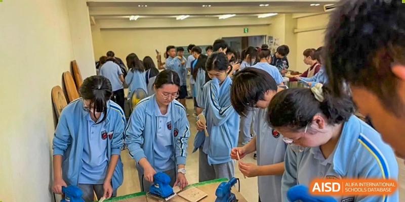 Students in blue uniforms work on a woodworking project using hand tools in a classroom at Wuxi Foreign Language School International Curriculum Center.