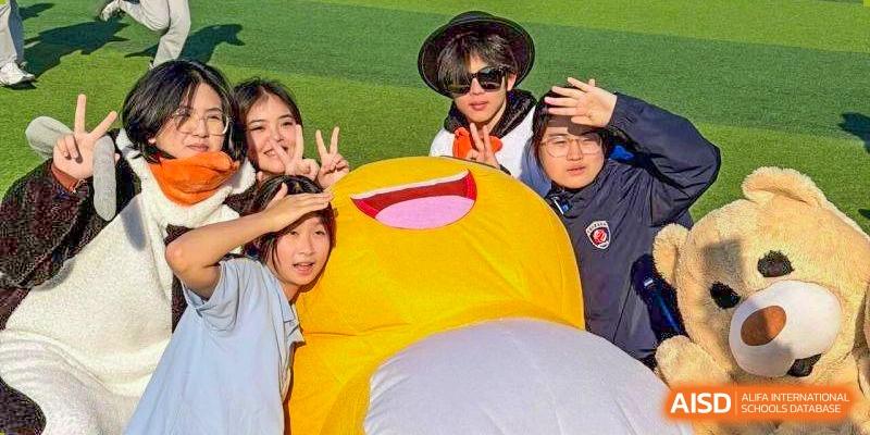 Students smile and pose next to a large, round yellow mascot character on a field at Wuxi Foreign Language School International Curriculum Center.