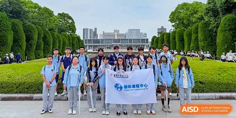Students hold a white school banner while posing in front of a large civic building for Wuxi Foreign Language School International Curriculum Center.
