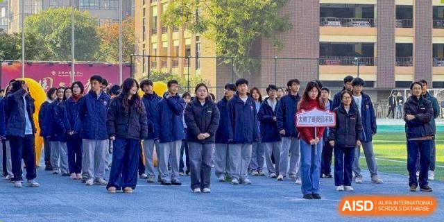 A group of students in dark blue winter jackets stand in formation on an outdoor court at Wuxi Foreign Language School International Curriculum Center.