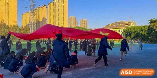 Students running beneath a large red flag during an outdoor ceremony at Wuxi Foreign Language School International Curriculum Center.