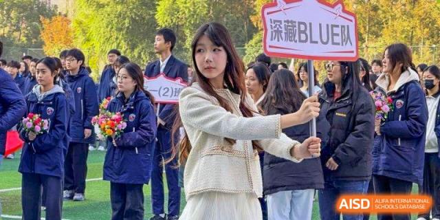 A female student in a white jacket participates in an outdoor school event or parade at Wuxi Foreign Language School International Curriculum Center.