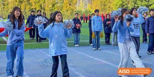 A student in a light blue star-patterned jacket leads a group on a field at Wuxi Foreign Language School International Curriculum Center.
